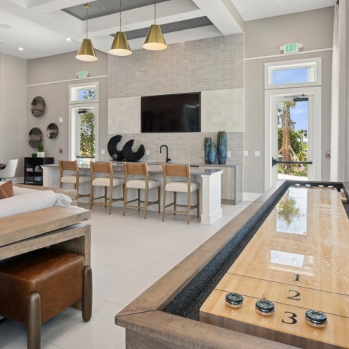 a clubroom with a tv, shuffleboard table, chairs and tables